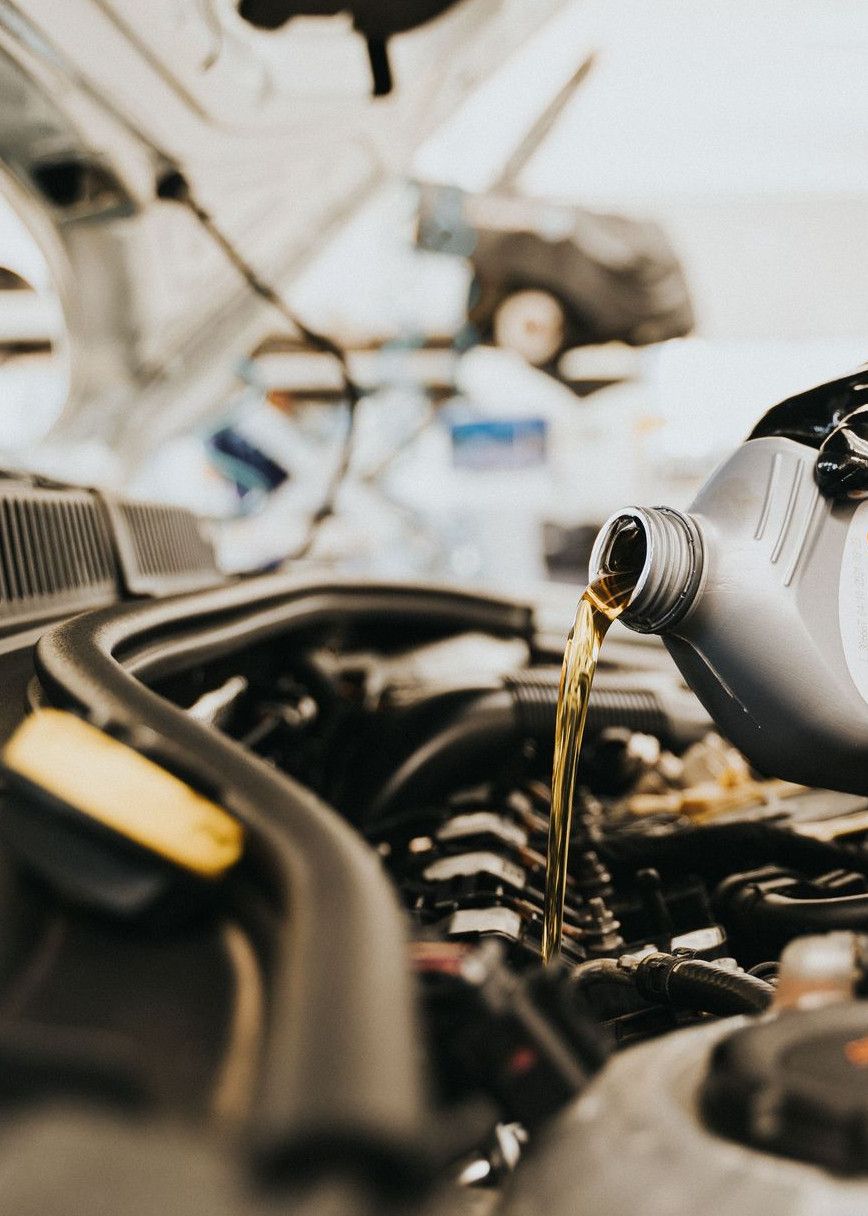 Close-up of a mechanic pouring engine oil into a car engine in an auto repair shop.